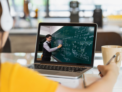 Profile of a woman looking at a laptop screen, which shows a teacher with a blackboard