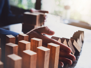 An adult hand stopping wooden blocks from falling onto other blocks.