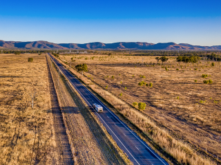 Image looking over a rural landscape with a caravan on the road down the centre and mountains in the distance